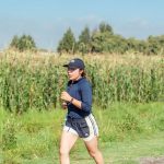Woman jogging along a rural path next to a cornfield, enjoying fitness in nature.